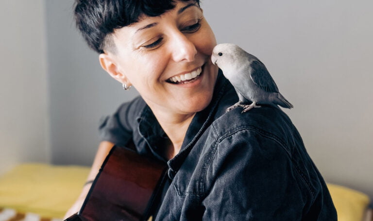 Happy woman and parrot bird enjoying together with guitar at home Owner and pet relationship, love concept